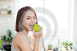 Happy Young Asian Woman Eating Green Apple on Kitchen. Diet. Die