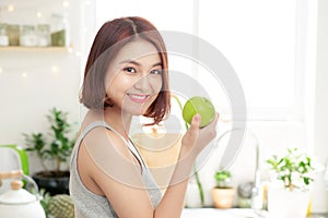 Happy Young Asian Woman Eating Green Apple on Kitchen. Diet. Die