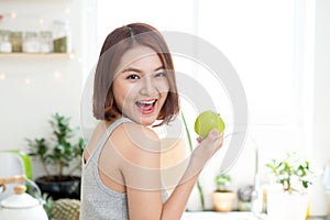 Happy Young Asian Woman Eating Green Apple on Kitchen. Diet. Dieting concept. Healthy food