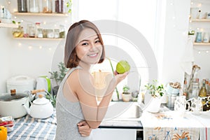 Happy Young Asian Woman Eating Green Apple on Kitchen. Diet.