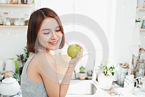 Happy Young Asian Woman Eating Green Apple on Kitchen. Diet. Die