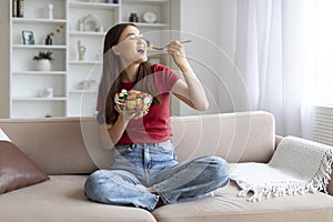 Happy young asian woman enjoying fresh salad bowl at home