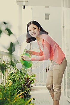 Happy Young Asian Woman housewife Watering flowers On Balcony