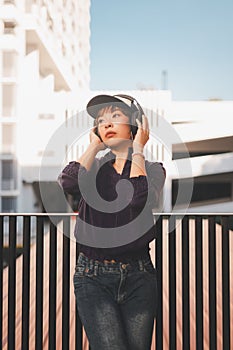 Happy young asian woman listening to music and having fun with headphones on the street.