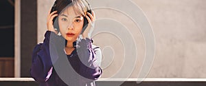 Happy young asian woman listening to music with headphones and looking at camera on the street. Banner background.