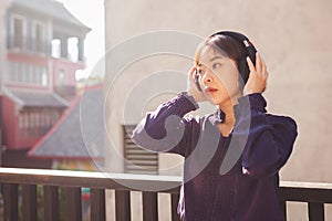 Happy young asian woman listening to music with headphones on the street.