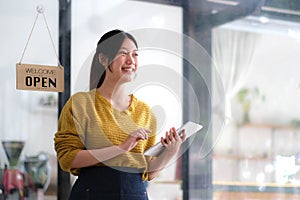 Happy young Asian woman owner standing holding a tablet with open sign board.