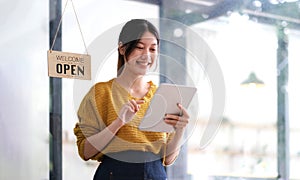 Happy young Asian woman owner standing holding a tablet with open sign board.