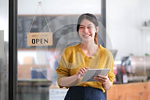 Happy young Asian woman owner standing holding a tablet with open sign board.