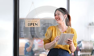 Happy young Asian woman owner standing holding a tablet with open sign board.