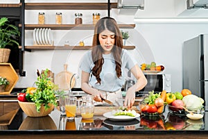 A happy young Asian woman preparing a healthy salad with fresh vegetables on a cutting board in the home kitchen. Food cooking.