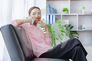 Happy young Asian woman relaxing at home sitting on sofa and using mobile smartphone using social media,