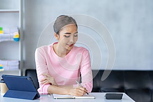 Happy young Asian woman relaxing at home sitting on sofa and using mobile smartphone using social media,