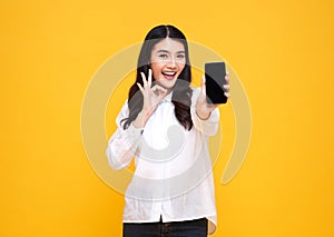 Happy young Asian woman showing at blank screen mobile phone and hand gesture ok isolated over yellow background