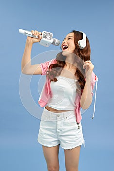 Happy young Asian woman singing with microphone sing and headphone over blue background