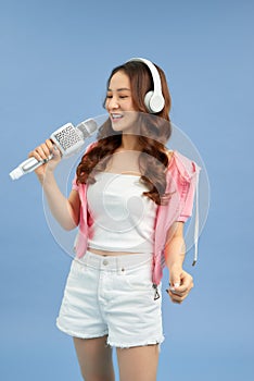 Happy young Asian woman singing with microphone sing and headphone over blue background