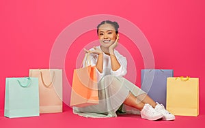 Happy young asian woman sitting on floor surrounded by colorful shopping bags