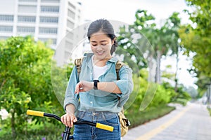 Happy young asian woman with smart watch riding bicycle on city street