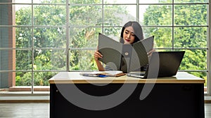 Happy young Asian woman smiling looking checking data on file binder in living room with copy space