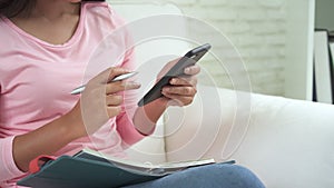 Happy young asian woman studying at home reading an sms or text message on her mobile phone with smile sitting on the couch.