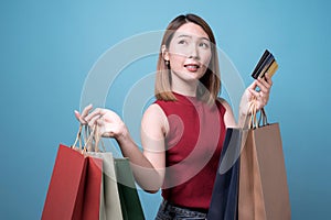 Happy young Asian woman in sunglasses holding credit card and colorful shopping bags