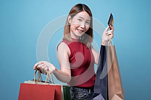 Happy young Asian woman in sunglasses holding credit card and colorful shopping bags