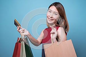 Happy young Asian woman in sunglasses holding credit card and colorful shopping bags