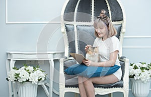 Happy young asian woman with tablet computer in her hands petting kitten sitting on sofa,University colleague student study online