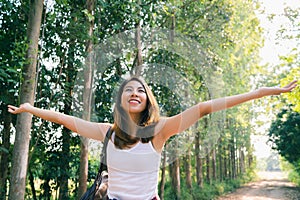 Happy young Asian woman traveler with backpack walking in forest. Hiker Asian woman with backpack walking on path in summer forest