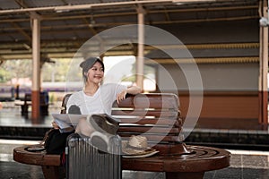 Happy young asian woman traveler or backpacker using map choose where to travel with luggage at train station, summer