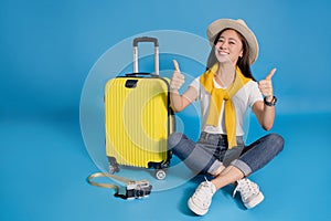 Happy young asian woman traveler sitting near a yellow suitcase on a blue background