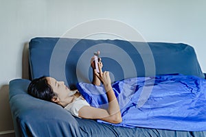 Happy Young Asian Woman Using  Mobile Phone Chatting While Sitting on Sofa at Home, Work from Home