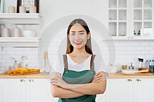 Happy young asian woman wearing apron and standing in kitchen room