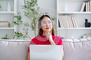 Happy young Asian woman wearing eyeglasses using laptop