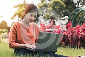 Happy young asian woman working with her laptop and relax on a grass in the park outdoors on vacation time