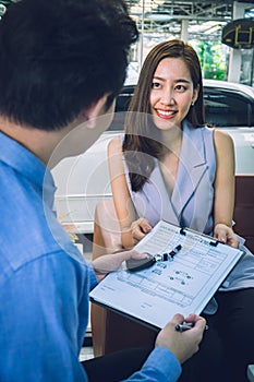 Happy young attractive Asian millennial girl getting a car key from a salesman at car dealership office. Film tone effected. -