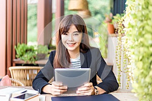 Happy young attractive business woman in her casual suit smiling at camera while working on her computer tablet at outdoor patio