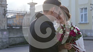 Happy young attractive wedding couple softly embracing and smiling near the church. Camera movement in slow motion