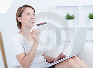 Happy young attractive woman shopping online via laptop computer, using credit card at home