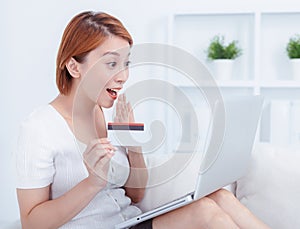 Happy young attractive woman shopping online via laptop computer, using credit card at home