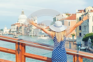 Happy young attractive woman of venice italy rising hands grand canal view blue polka dot outfit