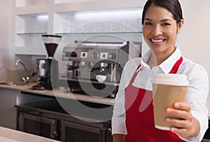 Happy young barista offering cup of coffee to go smiling at camera