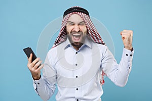 Happy young bearded arabian muslim man in keffiyeh kafiya ring igal agal casual clothes isolated on pastel blue