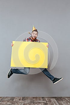 Happy young bearded birthday man holding copyspace board jumping