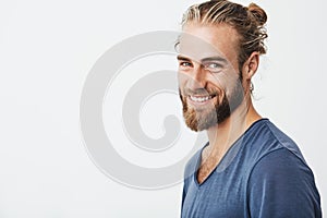 Happy young bearded guy with fashionable hairstyle and beard looking at camera, brightfully smiling with teeth, being