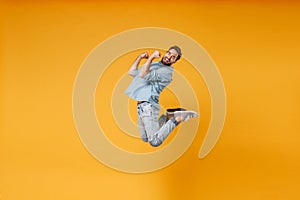 Happy young bearded man in casual blue shirt posing isolated on yellow orange background, studio portrait. People