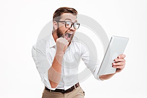 Happy young bearded man using tablet computer make winner gesture.