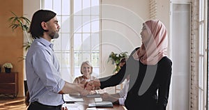 Happy young bearded manager shaking hands with smiling arab employee.