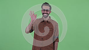 Happy young bearded Persian hipster man waving hand