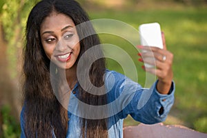 Happy young beautiful African woman taking selfie at the park